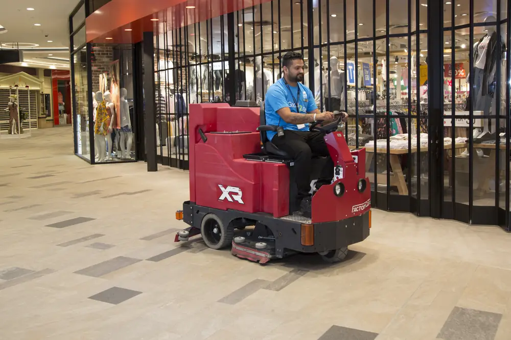 Westralian cleaner driving a ride-on floor scrubber through a shopping mall